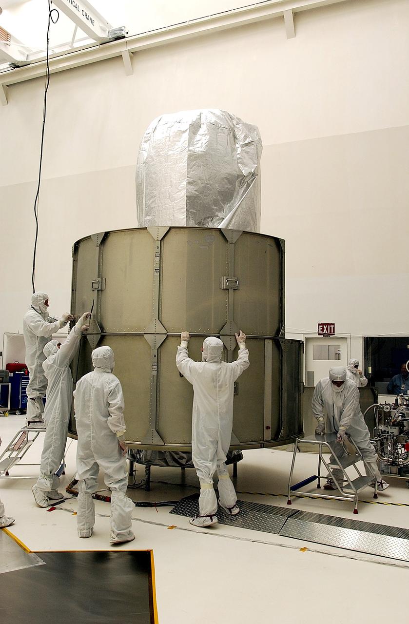 KENNEDY SPACE CENTER, FLA.  - Workers at Hangar A&E, Cape Canaveral Air Force Station, place the middle row of panels to encapsulate the Space Infrared Telescope Facility (SIRTF).  The spacecraft will be transported to Launch Complex 17-B for mating with its launch vehicle, the Delta II rocket.   SIRTF consists of three cryogenically cooled science instruments and an 0.85-meter telescope, and is one of NASA's largest infrared telescopes to be launched.  SIRTF will obtain images and spectra by detecting the infrared energy, or heat, radiated by objects in space. Most of this infrared radiation is blocked by the Earth's atmosphere and cannot be observed from the ground.