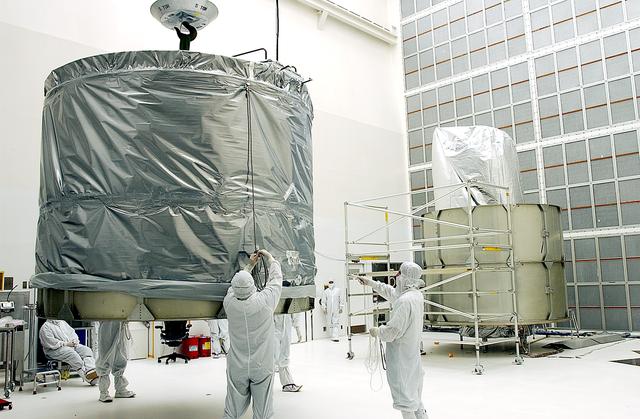 NASA image: KENNEDY SPACE CENTER, FLA.  - Workers at Hangar A&E, Cape Canaveral Air Force Station, lift the upper canister to move it to the Space Infrared Telescope Facility (SIRTF) at right.  After encapsulation, the spacecraft will be transported to Launch Complex 17-B for mating with its launch vehicle, the Delta II rocket.   SIRTF consists of three cryogenically cooled science instruments and an 0.85-meter telescope, and is one of NASA's largest infrared telescopes to be launched.  SIRTF will obtain images and spectra by detecting the infrared energy, or heat, radiated by objects in space. Most of this infrared radiation is blocked by the Earth's atmosphere and cannot be observed from the ground.