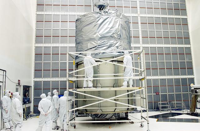 NASA image: KENNEDY SPACE CENTER, FLA.  -  Working from a stand, technicians fasten the upper portion of the canister to the middle panels around the Space Infrared Telescope Facility (SIRTF).  The spacecraft will be transported to Launch Complex 17-B for mating with its launch vehicle, the Delta II rocket.   SIRTF consists of three cryogenically cooled science instruments and an 0.85-meter telescope, and is one of NASA's largest infrared telescopes to be launched.  SIRTF will obtain images and spectra by detecting the infrared energy, or heat, radiated by objects in space. Most of this infrared radiation is blocked by the Earth's atmosphere and cannot be observed from the ground.