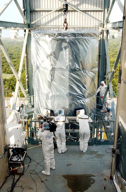 NASA image: KENNEDY SPACE CENTER, FLA.  -  Workers on the mobile service tower on Launch Pad 17-B, Cape Canaveral Air Force Station, wait for the Space Infrared Telescope Facility (SIRTF) to reach their level.  SIRTF will be attached to the Delta II rocket and encapsulated in its fairing before launch.   Consisting of three cryogenically cooled science instruments and an 0.85-meter telescope, SIRTF is one of NASA’s largest infrared telescopes to be launched.  It is the fourth and final element in NASA’s family of orbiting “Great Observatories.”  SIRTF will obtain images and spectra by detecting the infrared energy, or heat, radiated by objects in space. Most of this infrared radiation is blocked by the Earth's atmosphere and cannot be observed from the ground.