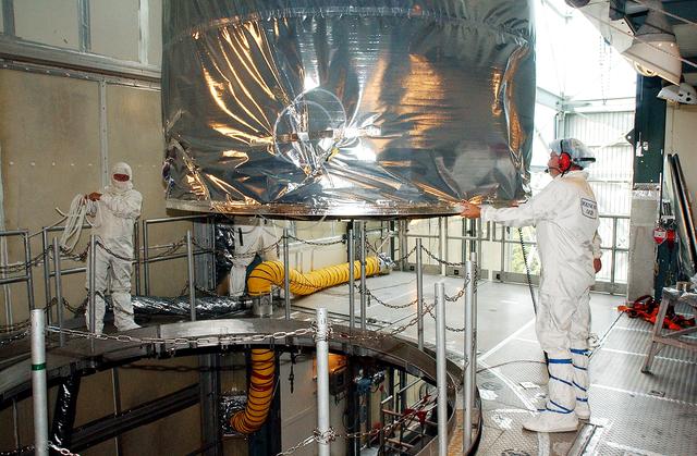 NASA image: KENNEDY SPACE CENTER, FLA.  -  Workers on the mobile service tower on Launch Pad 17-B, Cape Canaveral Air Force Station, help guide the Space Infrared Telescope Facility (SIRTF) toward the opening in the foreground.  SIRTF will be attached to the Delta II rocket and encapsulated in its fairing before launch.   Consisting of three cryogenically cooled science instruments and an 0.85-meter telescope, SIRTF is one of NASA’s largest infrared telescopes to be launched.  It is the fourth and final element in NASA’s family of orbiting “Great Observatories.”  SIRTF will obtain images and spectra by detecting the infrared energy, or heat, radiated by objects in space. Most of this infrared radiation is blocked by the Earth's atmosphere and cannot be observed from the ground.