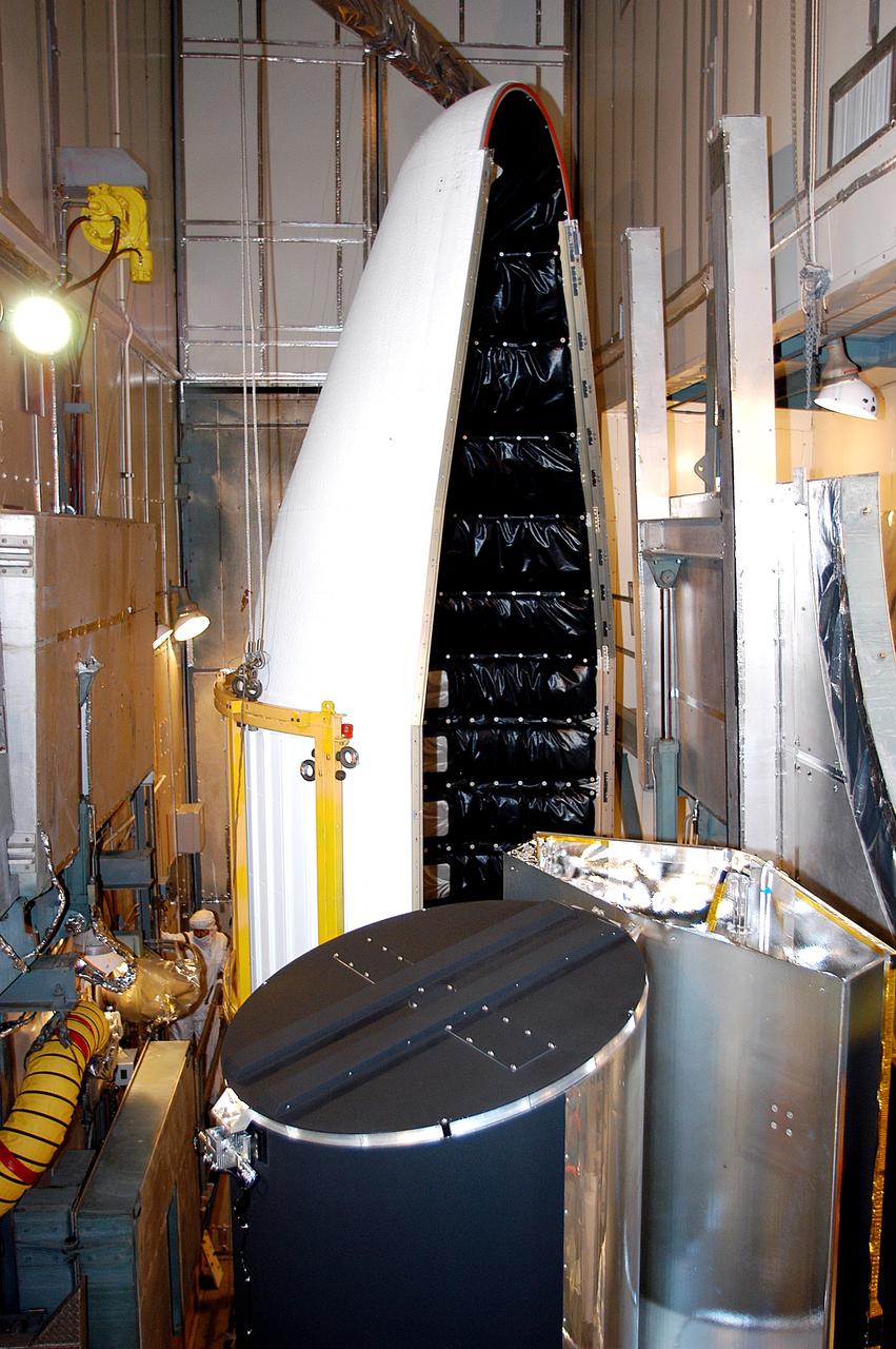 KENNEDY SPACE CENTER, FLA.  - In the mobile service tower on Launch Pad 17-B, Cape Canaveral Air Force Station, the first half of the fairing (background) moves toward the Space Infrared Telescope Facility (foreground) for encapsulation. SIRTF will obtain images and spectra by detecting the infrared energy, or heat, radiated by objects in space. Consisting of a 0.85-meter telescope and three cryogenically cooled science instruments, SIRTF will be the largest infrared telescope ever launched into space. It is the fourth and final element in NASA’s family of orbiting “Great Observatories.” Its highly sensitive instruments will give a unique view of the Universe and peer into regions of space that are hidden from optical telescopes.