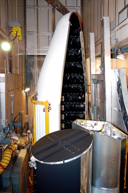 NASA image: KENNEDY SPACE CENTER, FLA.  - In the mobile service tower on Launch Pad 17-B, Cape Canaveral Air Force Station, the first half of the fairing (background) moves toward the Space Infrared Telescope Facility (foreground) for encapsulation. SIRTF will obtain images and spectra by detecting the infrared energy, or heat, radiated by objects in space. Consisting of a 0.85-meter telescope and three cryogenically cooled science instruments, SIRTF will be the largest infrared telescope ever launched into space. It is the fourth and final element in NASA’s family of orbiting “Great Observatories.” Its highly sensitive instruments will give a unique view of the Universe and peer into regions of space that are hidden from optical telescopes.