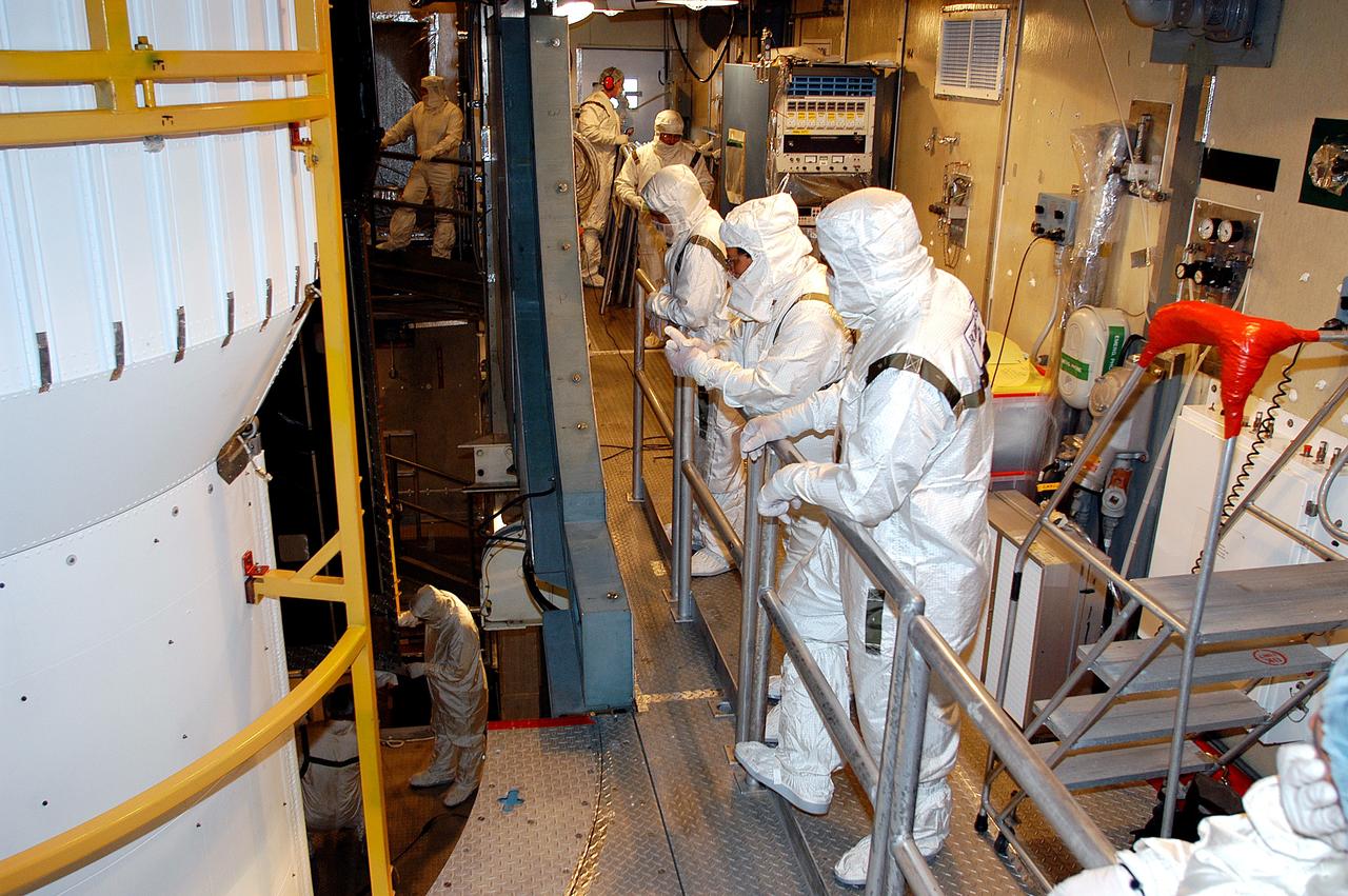 KENNEDY SPACE CENTER, FLA.  - In the mobile service tower on Launch Pad 17-B, Cape Canaveral Air Force Station, workers watch as the first half of the fairing moves closer around the Space Infrared Telescope Facility (SIRTF). SIRTF will obtain images and spectra by detecting the infrared energy, or heat, radiated by objects in space. Consisting of a 0.85-meter telescope and three cryogenically cooled science instruments, SIRTF will be the largest infrared telescope ever launched into space. It is the fourth and final element in NASA’s family of orbiting “Great Observatories.” Its highly sensitive instruments will give a unique view of the Universe and peer into regions of space that are hidden from optical telescopes.