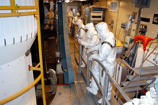 NASA image: KENNEDY SPACE CENTER, FLA.  - In the mobile service tower on Launch Pad 17-B, Cape Canaveral Air Force Station, workers watch as the first half of the fairing moves closer around the Space Infrared Telescope Facility (SIRTF). SIRTF will obtain images and spectra by detecting the infrared energy, or heat, radiated by objects in space. Consisting of a 0.85-meter telescope and three cryogenically cooled science instruments, SIRTF will be the largest infrared telescope ever launched into space. It is the fourth and final element in NASA’s family of orbiting “Great Observatories.” Its highly sensitive instruments will give a unique view of the Universe and peer into regions of space that are hidden from optical telescopes.