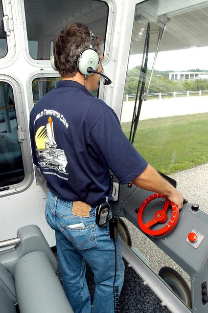 NASA image: KENNEDY SPACE CENTER, FLA.  - Inside the cab of crawler-transporter (CT) number 2, driver Sam Dove, with United Space Alliance, operates the vehicle on a test run to the launch pad.  The CT recently underwent modifications to the cab.   The CT is transporting a Mobile Launch Platform (MLP).  The CT moves Space Shuttle vehicles, situated on the MLP, between the VAB and launch pad.  Moving on four double-tracked crawlers, the CT uses a laser guidance system and a leveling system for the journey that keeps the top of a Space Shuttle vertical within plus- or minus-10 minutes of arc.  The system enables the CT-MLP-Shuttle to negotiate the ramp leading to the launch pads and keep the load level.  Unloaded, the CT weighs 6 million pounds.  Seen on top of the MLP are two tail service masts that support the fluid, gas and electrical requirements of the orbiter’s liquid oxygen and liquid hydrogen aft umbilicals.