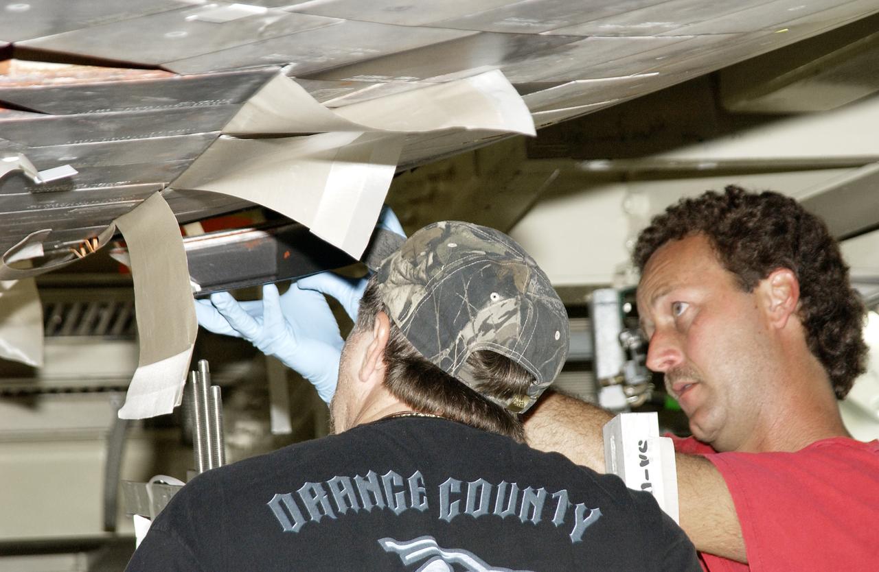 Workers make a tile-fit check on the underside of the orbiter Discovery in the Orbiter Processing Facility. The vehicle has undergone Orbiter Major Modifications in the past year, a process that includes the tile check.