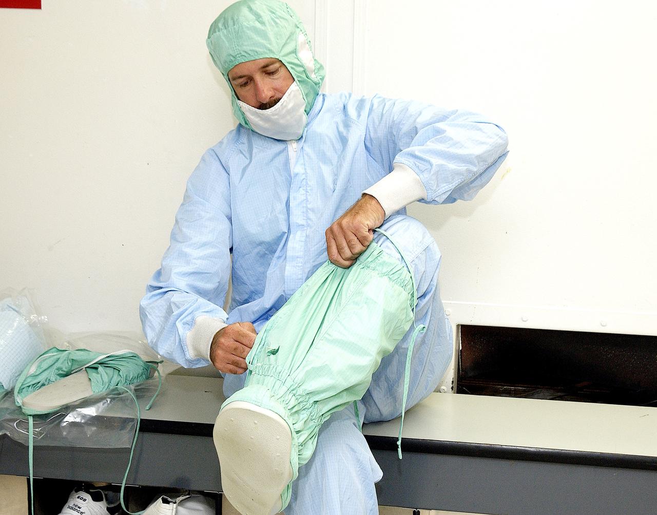 KENNEDY SPACE CENTER, FLA. -  A KSC employee dons the foot and leg covers of a "bunny suit," part of standard clean room apparel, before entering a clean room. The apparel is designed to cover the hair, clothing and shoes of employees to prevent particulate matter from contaminating the space flight hardware being stored or processed in the clean room and is one aspect of KSC's Foreign Object Debris (FOD) control program, an important safety initiative.