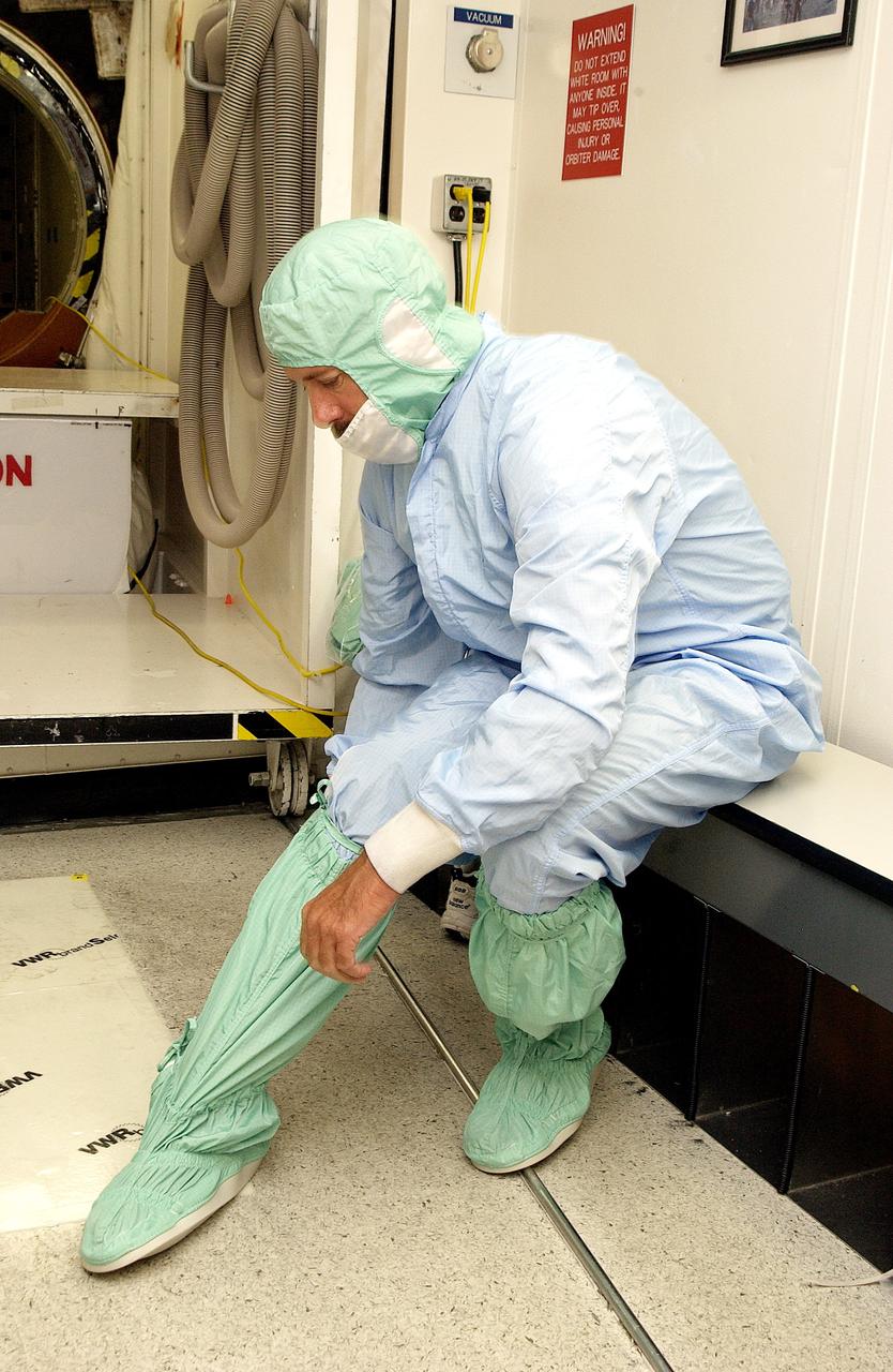 KENNEDY SPACE CENTER, FLA. -  A KSC employee secures a foot and leg cover of his "bunny suit," part of standard clean room apparel, before entering a clean room. The apparel is designed to cover the hair, clothing and shoes of employees to prevent particulate matter from contaminating the space flight hardware being stored or processed in the clean room and is one aspect of KSC's Foreign Object Debris (FOD) control program, an important safety initiative.