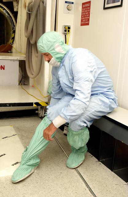 NASA image: KENNEDY SPACE CENTER, FLA. -  A KSC employee secures a foot and leg cover of his "bunny suit," part of standard clean room apparel, before entering a clean room. The apparel is designed to cover the hair, clothing and shoes of employees to prevent particulate matter from contaminating the space flight hardware being stored or processed in the clean room and is one aspect of KSC's Foreign Object Debris (FOD) control program, an important safety initiative.