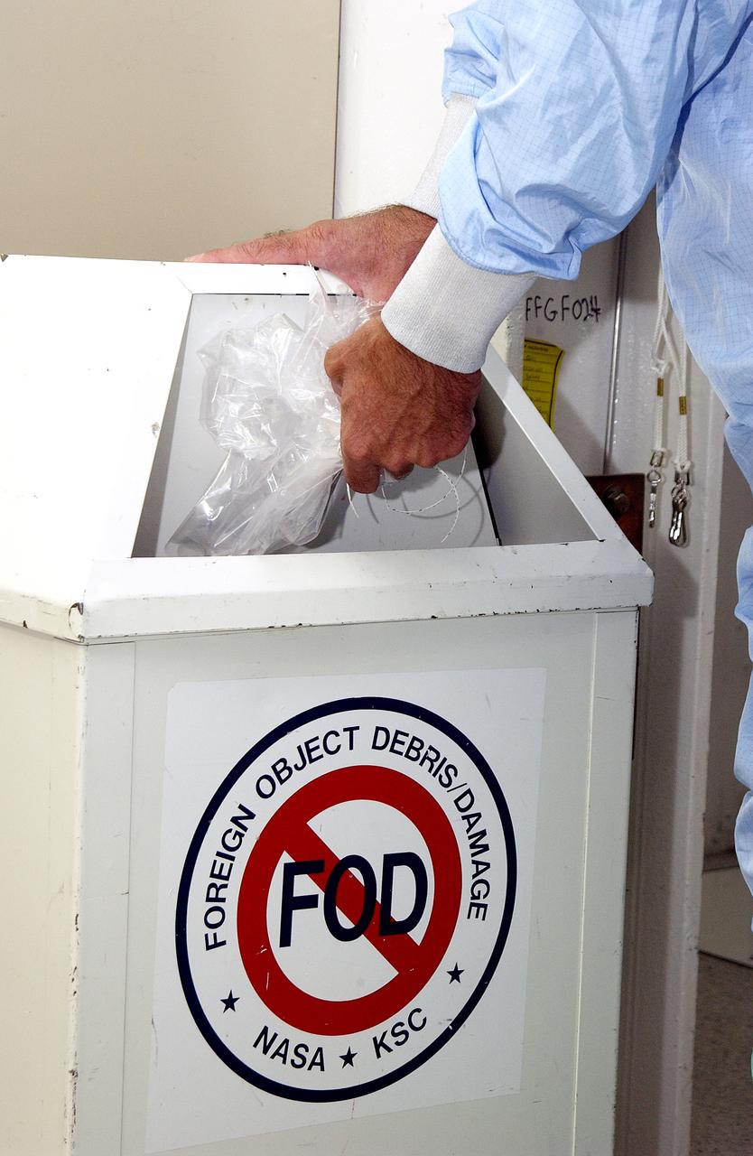 KENNEDY SPACE CENTER, FLA. -  A KSC employee dressed in a "bunny suit," standard clean room apparel, disposes of some waste material into a container designated for the purpose. The apparel is designed to cover the hair, clothing and shoes of employees entering a clean room to prevent particulate matter from contaminating the space flight hardware being stored or processed in the room. The suit and container are both part of KSC's Foreign Object Debris (FOD) control program, an important safety initiative.