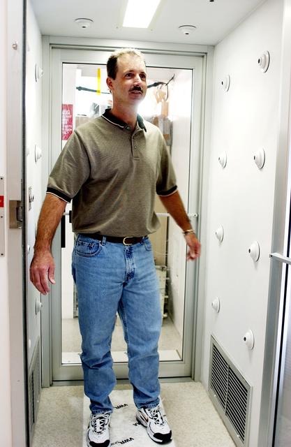 NASA image: KENNEDY SPACE CENTER, FLA. -  A KSC employee uses a clean-air shower before entering a clean room.  Streams of pressurized air directed at the occupant from nozzles in the chamber's ceiling and walls are designed to dislodge particulate matter from hair, clothing and shoes.  The adhesive mat on the floor captures soil from shoe soles, as well as particles that fall on its surface.  Particulate matter has the potential to contaminate the space flight hardware being stored or processed in the clean room. The shower is part of KSC's Foreign Object Debris (FOD) control program, an important safety initiative.
