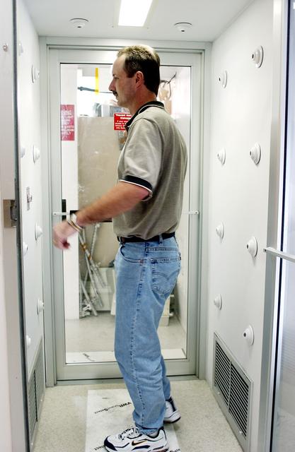 NASA image: KENNEDY SPACE CENTER, FLA. -  A KSC employee uses a clean-air shower before entering a clean room.  Streams of pressurized air directed at the occupant from nozzles in the chamber's ceiling and walls are designed to dislodge particulate matter from hair, clothing and shoes.  The adhesive mat on the floor captures soil from shoe soles, as well as particles that fall on its surface.  Particulate matter has the potential to contaminate the space flight hardware being stored or processed in the clean room. The shower is part of KSC's Foreign Object Debris (FOD) control program, an important safety initiative.