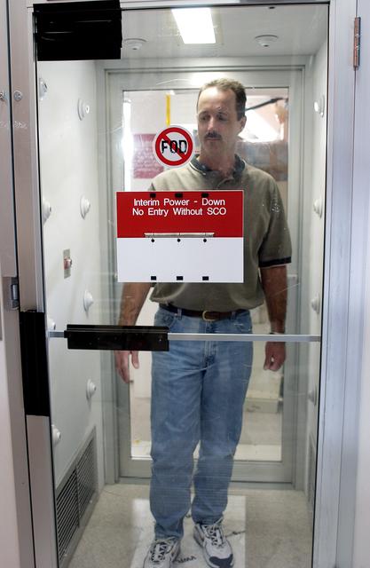 NASA image: KENNEDY SPACE CENTER, FLA. -  A KSC employee uses a clean-air shower before entering a clean room.  Streams of pressurized air directed at the occupant from nozzles in the chamber's ceiling and walls are designed to dislodge particulate matter from hair, clothing and shoes.  The adhesive mat on the floor captures soil from shoe soles, as well as particles that fall on its surface.  Particulate matter has the potential to contaminate the space flight hardware being stored or processed in the clean room. The shower is part of KSC's Foreign Object Debris (FOD) control program, an important safety initiative.