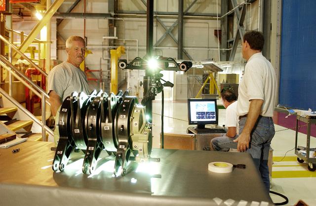NASA image: KENNEDY SPACE CENTER, FLA. - Boeing workers perform a 3D digital scan of the actuator on the table.  At left is Dan Clark.  At right are Alden Pitard (seated at computer) and  John Macke, from Boeing, St. Louis.  .  There are two actuators per engine on the Shuttle, one for pitch motion and one for yaw motion. The Space Shuttle Main Engine hydraulic servoactuators are used to gimbal the main engine.