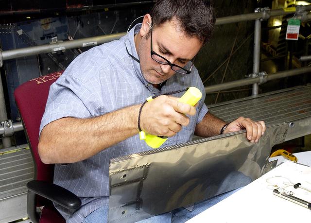 NASA image: KENNEDY SPACE CENTER, FLA. - In the Orbiter Processing Facility, John Newport, with United Space Alliance, inspects a piece of equipment for spar installation on the wing of the orbiter Atlantis.  Reinforced Carbon Carbon (RCC) panels are mechanically attached to the wing with a series of floating joints - spars - to reduce loading on the panels caused by wing deflections. The aluminum and the metallic attachments are protected from exceeding temperature limits by internal insulation.