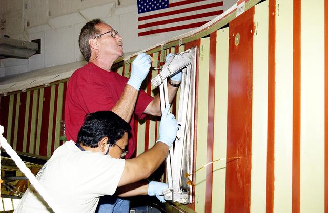NASA image: KENNEDY SPACE CENTER, FLA. - In the Orbiter Processing Facility, Mike Hyatt (above) and Saul Ngy (below), with United Space Alliance, install a spar on the wing of the orbiter Atlantis.  Reinforced Carbon Carbon (RCC) panels are mechanically attached to the wing with a series of floating joints - spars - to reduce loading on the panels caused by wing deflections. The aluminum and the metallic attachments are protected from exceeding temperature limits by internal insulation.