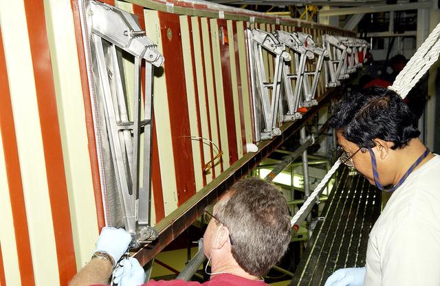 NASA image: KENNEDY SPACE CENTER, FLA. - In the Orbiter Processing Facility, Mike Hyatt (left) and Saul Ngy (right), with United Space Alliance, finish installing a spar on the wing of the orbiter Atlantis.  Reinforced Carbon Carbon (RCC) panels are mechanically attached to the wing with a series of floating joints - spars - to reduce loading on the panels caused by wing deflections. The aluminum and the metallic attachments are protected from exceeding temperature limits by internal insulation.