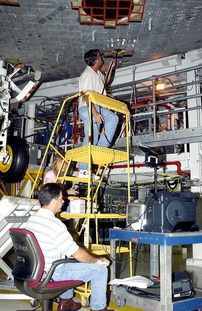 NASA image: KENNEDY SPACE CENTER, FLA. -   In the Orbiter Processing Facility, while Greg Harlow, with United Space Alliance (USA) (above) threads a camera under the tiles of the orbiter Endeavour, Peggy Ritchie, USA, (behind the stand) and NASA’s Richard Parker (seated) watch the images on a monitor to inspect for corrosion.