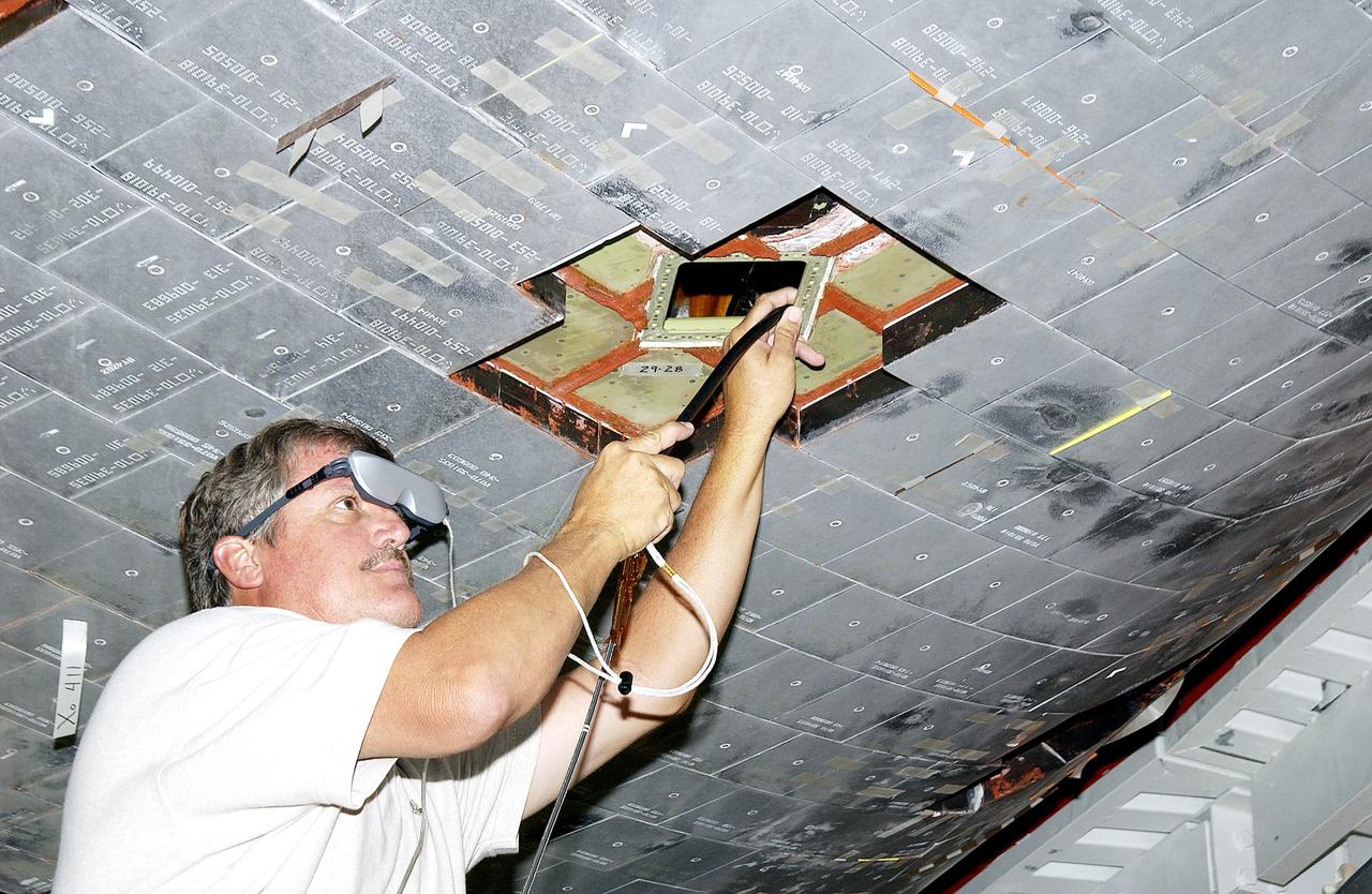 KENNEDY SPACE CENTER, FLA. -  In the Orbiter Processing Facility, Greg Harlow, with United Space Alliance (USA), threads a camera under the tiles of the orbiter Endeavour to inspect for corrosion.