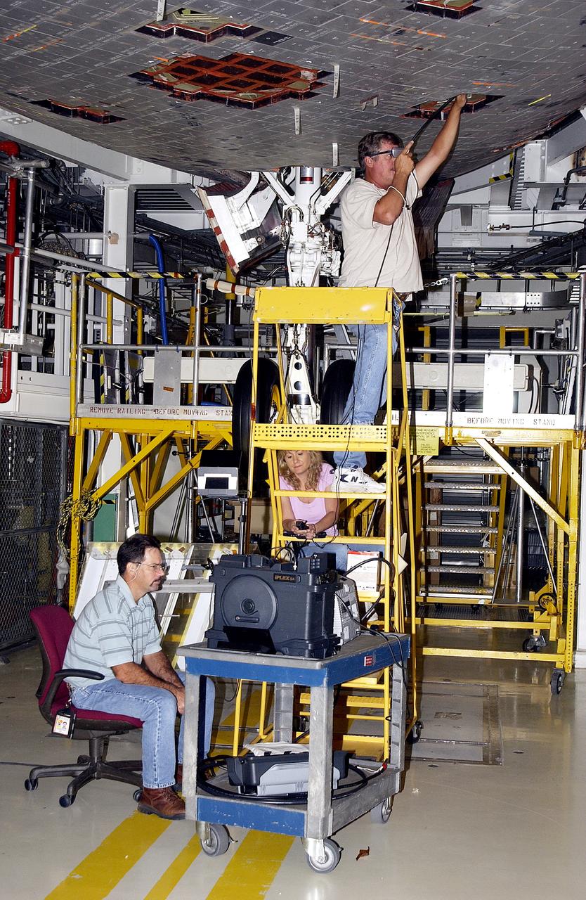 KENNEDY SPACE CENTER, FLA. -  In the Orbiter Processing Facility, while Greg Harlow, with United Space Alliance (USA), (above) threads a camera under the tiles of the orbiter Endeavour, Peggy Ritchie, with USA, (behind the stand) and NASA’s Richard Parker watch the images on a monitor to inspect for corrosion.