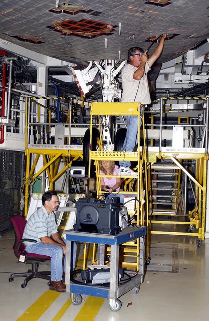 NASA image: KENNEDY SPACE CENTER, FLA. -  In the Orbiter Processing Facility, while Greg Harlow, with United Space Alliance (USA), (above) threads a camera under the tiles of the orbiter Endeavour, Peggy Ritchie, with USA, (behind the stand) and NASA’s Richard Parker watch the images on a monitor to inspect for corrosion.