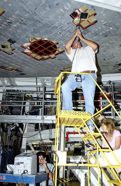 NASA image: KENNEDY SPACE CENTER, FLA. - In the Orbiter Processing Facility, while Greg Harlow, with United Space Alliance (USA), (above) threads a camera under the tiles of the orbiter Endeavour, NASA’s Richard Parker (below left) and Peggy Ritchie, with USA, (at right) watch the images on a monitor to inspect for corrosion.