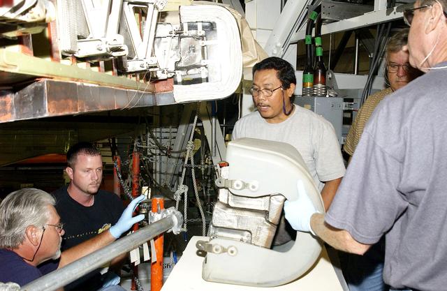 NASA image: KENNEDY SPACE CENTER, FLA. - In the Orbiter Processing Facility, United Space Alliance workers, from center, left to right, Saul Ngy, Jerry Belt and Mike Hyatt, prepare to attach a Reinforced Carbon Carbon (RCC) panel (on the table) to the leading edge of the wing of the orbiter Atlantis.  The gray carbon composite RCC panels have sufficient strength to withstand the aerodynamic forces experienced during launch and reentry, which can reach as high as 800 pounds per square foot. The operating range of RCC is from minus 250º F to about 3,000º F, the temperature produced by friction with the atmosphere during reentry.