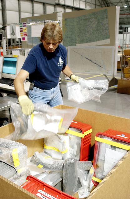 NASA image: KENNEDY SPACE CENTER, FLA. - In the Columbia Debris Hangar, Jack Nowling transfers bags with debris pieces into a storage box.  About 83,000 pieces of debris were shipped to KSC during search and recovery efforts in East Texas. That represents about 38 percent of the dry weight of Columbia, equaling almost 85,000 pounds.  An area of the Vehicle Assembly Building is being prepared to store the debris.