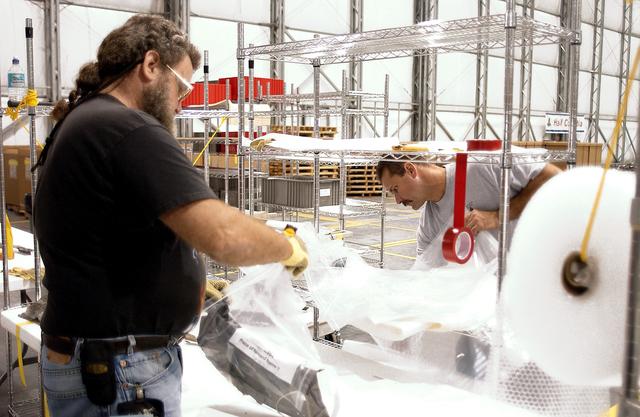 NASA image: KENNEDY SPACE CENTER, FLA. -  In the Columbia Debris Hangar, Larry Tarver (left) and Don Eitel bag and wrap pieces of debris to be packed into storage boxes.  About 83,000 pieces of debris were shipped to KSC during search and recovery efforts in East Texas. That represents about 38 percent of the dry weight of Columbia, equaling almost 85,000 pounds.  An area of the Vehicle Assembly Building is being prepared to store the debris.