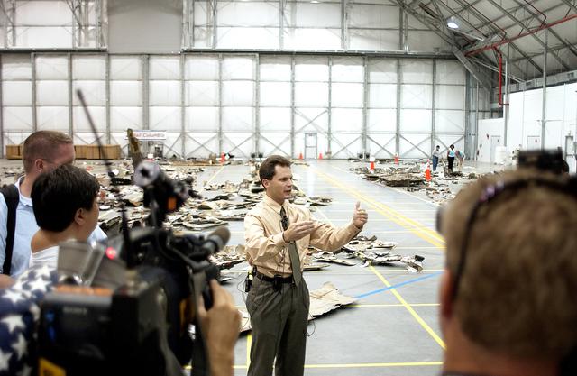 NASA image: KENNEDY SPACE CENTER, FLA. - In the Columbia Debris Hangar, Scott Thurston, NASA vehicle flow manager, addresses the media about efforts to pack the debris stored in the Columbia Debris Hangar.  More than 83,000  pieces of debris were shipped to KSC during search and recovery efforts in East Texas. That represents about 38 percent of the dry weight of Columbia, equaling almost 85,000 pounds. An area of the Vehicle Assembly Building is being prepared to store the debris permanently.