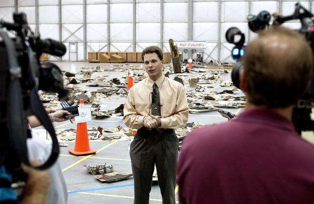 NASA image: KENNEDY SPACE CENTER, FLA. - In the Columbia Debris Hangar, Scott Thurston, NASA vehicle flow manager, addresses the media about efforts to pack the debris stored in the Columbia Debris Hangar.  More than 83,000  pieces of debris were shipped to KSC during search and recovery efforts in East Texas. That represents about 38 percent of the dry weight of Columbia, equaling almost 85,000 pounds. An area of the Vehicle Assembly Building is being prepared to store the debris permanently.