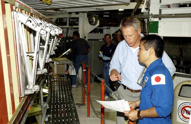 NASA image: KENNEDY SPACE CENTER, FLA. - Japanese astronaut Koichi Wakata (right) listens to William Gaetjens, with the Vehicle Integration Test Team (VITT), who is providing details about the spar installation (left) on the wing of the orbiter Atlantis.  Reinforced Carbon Carbon (RCC) panels are mechanically attached to the wing via the spars - a series of floating joints - to reduce loading on the panels caused by wing deflections. The aluminum and the metallic attachments are protected from exceeding temperature limits by internal insulation.