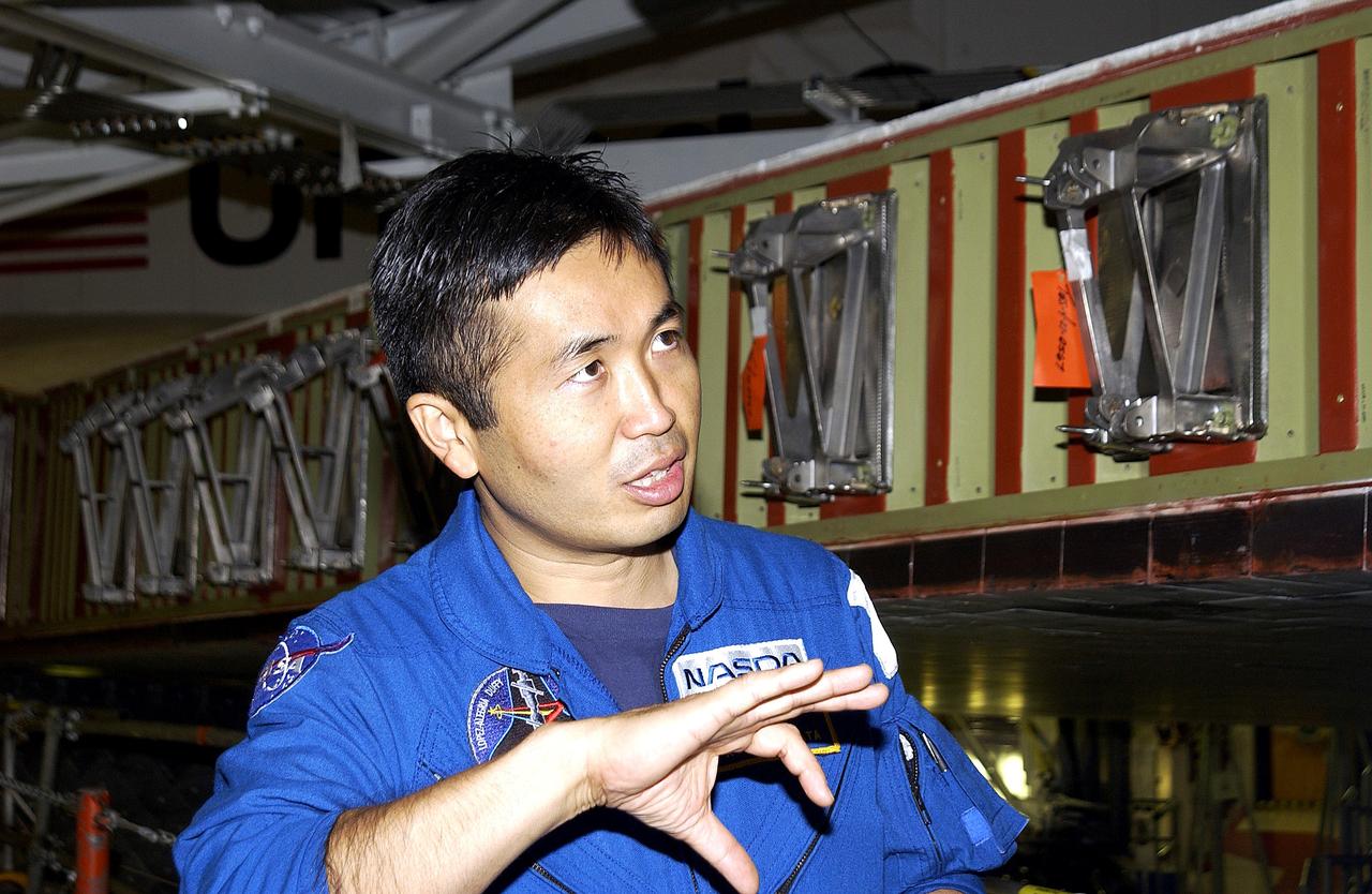 KENNEDY SPACE CENTER, FLA. - Japanese astronaut Koichi Wakata gestures as he examines the spar installation (behind him) on the wing of the orbiter Atlantis.  Reinforced Carbon Carbon (RCC) panels are mechanically attached to the wing via the spars - a series of floating joints - to reduce loading on the panels caused by wing deflections. The aluminum and the metallic attachments are protected from exceeding temperature limits by internal insulation.