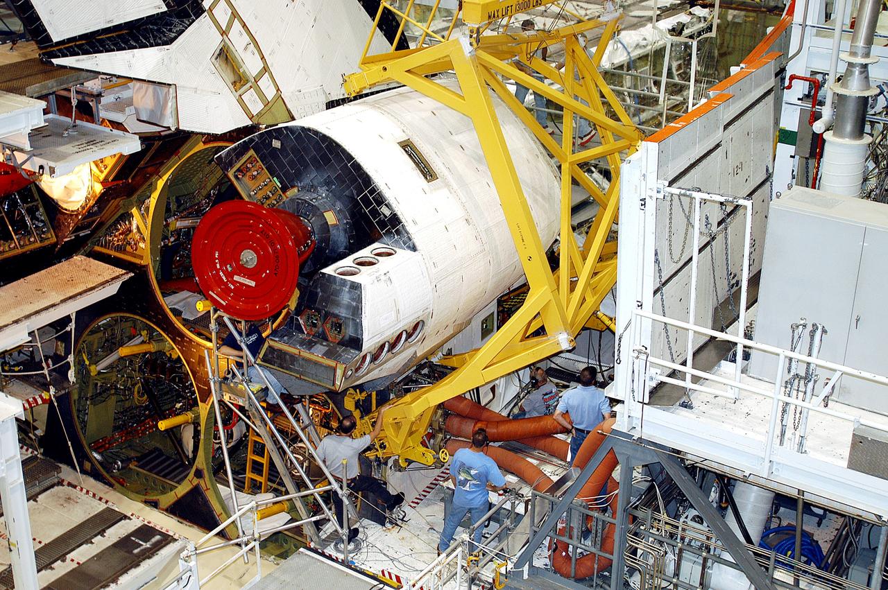 KENNEDY SPACE CENTER, FLA. - Workers in the Orbiter Processing Facility prepare to remove one of two orbital maneuvering system (OMS) pods from Endeavour. The OMS pods are attached to the upper aft fuselage left and right sides. Fabricated primarily of graphite epoxy composite and aluminum, each pod is 21.8 feet long and 11.37 feet wide at its aft end and 8.41 feet wide at its forward end, with a surface area of approximately 435 square feet. Each pod houses the Reaction Control System propulsion components used for inflight maneuvering and is attached to the aft fuselage with 11 bolts. OMS pods are removed during Orbiter Major Modifications. Once removed, the OMS pods undergo in-depth structural inspections, system checks and the thrusters are changed out.