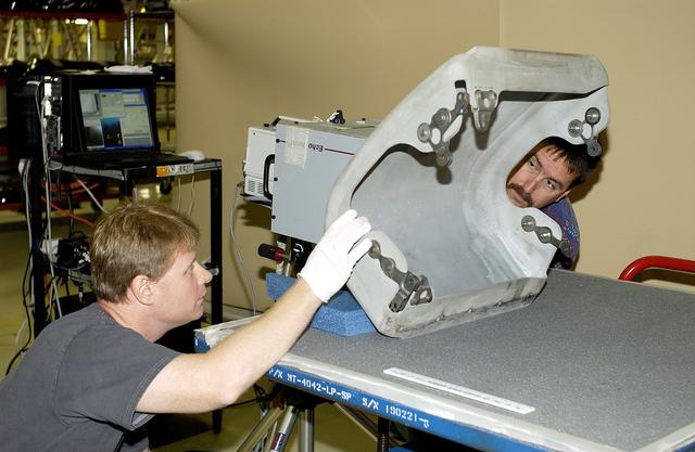 NASA image: KENNEDY SPACE CENTER, FLA. -  In the Orbiter Processing Facility,  Jim Landy (left), NDE specialist with United Space Alliance (USA), prepares to examine a Reinforced Carbon Carbon panel using flash thermography.  Helping out, at right, is Dan Phillips, also with USA.  Attached to the leading edge of the wing of the orbiters,  the gray carbon composite RCC panels have sufficient strength to withstand the aerodynamic forces experienced during launch and reentry, which can reach as high as 800 pounds per square foot.  The operating range of RCC is from minus 250º F to about 3,000º F, the temperature produced by friction with the atmosphere during reentry.
