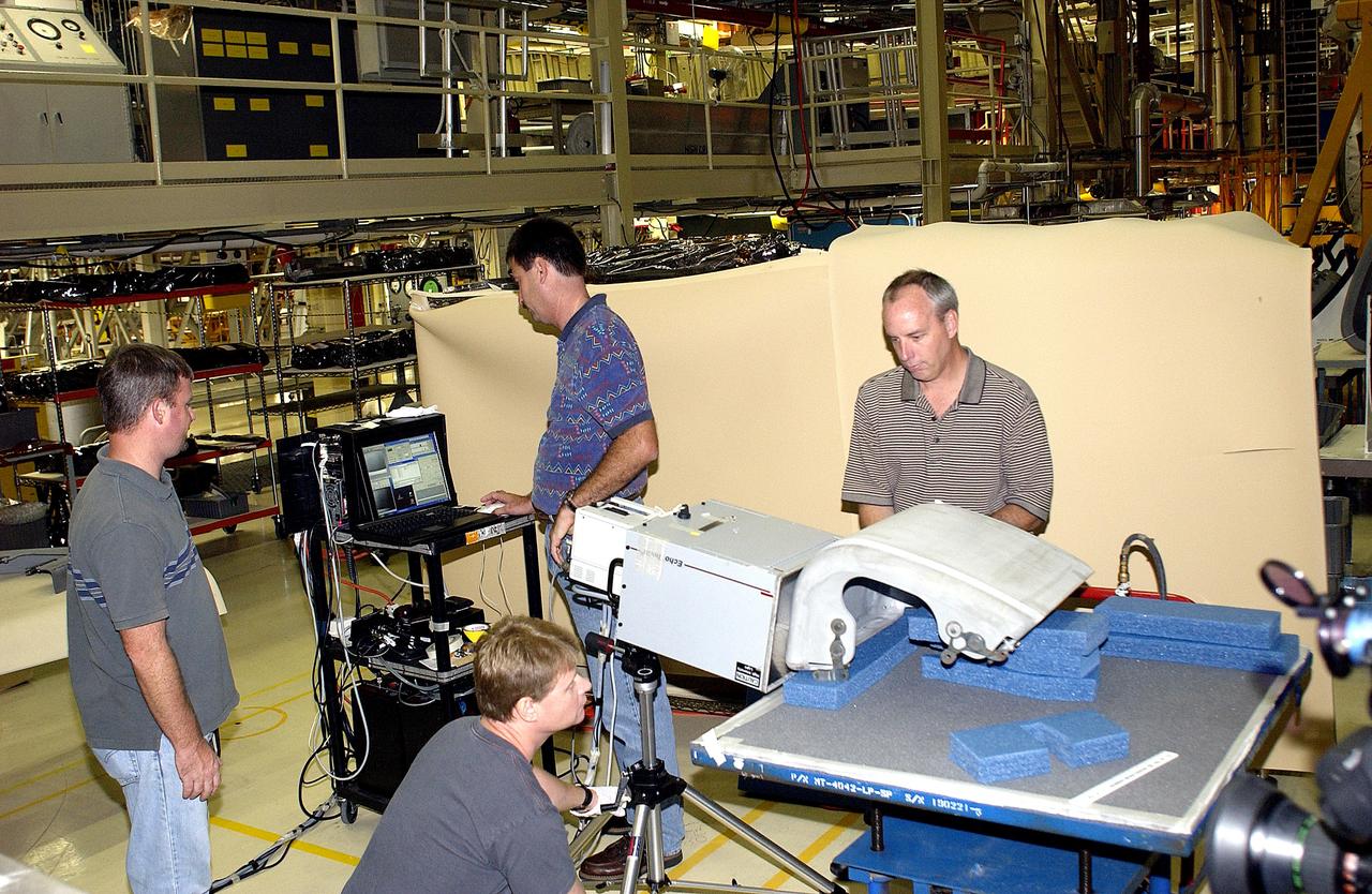 KENNEDY SPACE CENTER, FLA. - In the Orbiter Processing Facility, United Space Alliance workers share the task of examining  a Reinforced Carbon Carbon panel using flash thermography.  From left are Paul Ogletree, Jim Landy (kneeling), Dan Phillips and Dan Kenna.  Attached to the leading edge of the wing of the orbiters,  the gray carbon composite RCC panels have sufficient strength to withstand the aerodynamic forces experienced during launch and reentry, which can reach as high as 800 pounds per square foot.  The operating range of RCC is from minus 250º F to about 3,000º F, the temperature produced by friction with the atmosphere during reentry.