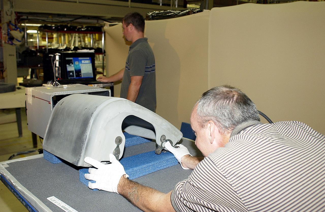 KENNEDY SPACE CENTER, FLA. -  In the Orbiter Processing Facility, United Space Alliance worker Dan Kenna (right) positions a Reinforced Carbon Carbon panel on the table to perform flash thermography.  In the background, Paul Ogletree observes the monitor.  Attached to the leading edge of the wing of the orbiters,  the gray carbon composite RCC panels have sufficient strength to withstand the aerodynamic forces experienced during launch and reentry, which can reach as high as 800 pounds per square foot.  The operating range of RCC is from minus 250º F to about 3,000º F, the temperature produced by friction with the atmosphere during reentry.