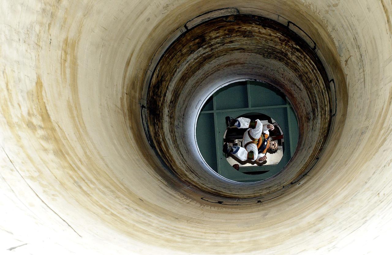 KENNEDY SPACE CENTER, FLA. -   Seen from below and through a solid rocket booster segment mockup, Jeff Thon, an SRB mechanic with United Space Alliance, tests the feasibility of a vertical solid rocket booster propellant grain inspection technique.  The inspection of segments is required as part of safety analysis.