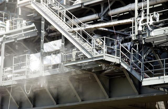 NASA image: KENNEDY SPACE CENTER, FLA. - Workers, covered in protective clothing and breathing apparatus, continue sandblasting on the Mobile Launcher Platform on Launch Pad 39A to remove corrosion before repainting.  Routine maintenance includes sandblasting and repainting as preventive means to minimize corrosion.