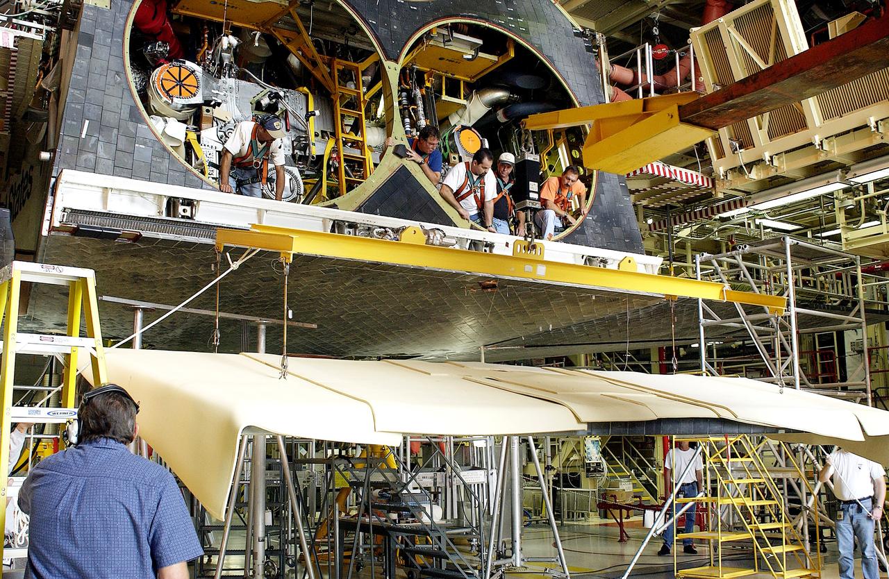 KENNEDY SPACE CENTER, FLA. - In the Orbiter Processing Facility, workers look down from spaces allotted for the main engines as the rear body flap is lifted for installation on the orbiter Discovery.  The body flap, which is temporarily under protective covering, attaches below the main engines.
