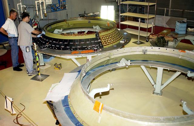 NASA image: KENNEDY SPACE CENTER, FLA. -  While Jay Beason (left), with United Space Alliance,  looks on, Jeremy Schwarz (front) and Tom Summers (behind), also with USA, place new tiles on the heat shield of main engine 1 for the orbiter Discovery.  A heat shield is a protective layer on a spacecraft designed to protect it from the high temperatures, usually those that result from aerobraking during reentry into the Earth’s atmosphere.