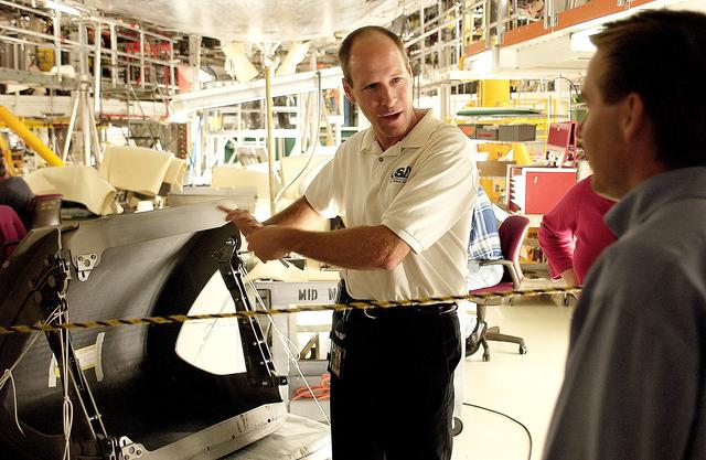 NASA image: KENNEDY SPACE CENTER, FLA. -  In the Orbiter Processing Facility, Rick Beckwith (center), an orbiter engineer with United Space Alliance, explains to the media the reinstallation of the Reinforced Carbon-Carbon panels on the orbiter Atlantis’ wing leading edge.  The media was invited to tour the OPF at KSC and to see the orbiter Atlantis as it is being prepared for Return to Flight.  Both local and national reporters representing print and TV networks were able to see work in progress on Atlantis, also including wiring inspections and checks of the engines in the Orbital Maneuvering System.