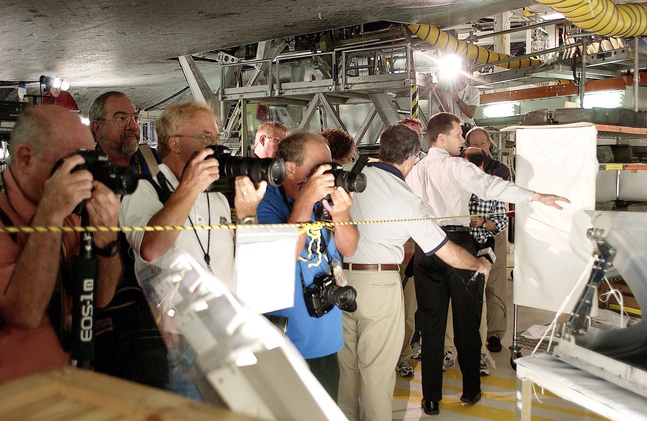 KENNEDY SPACE CENTER, FLA. -  In the Orbiter Processing Facility,  while a few photographers (left) set up for photos, NASA Vehicle Manager Scott Thurston (right, with arm extended) talks about the Reinforced Carbon-Carbon panel at right.   The media was invited to see the orbiter Atlantis as it is being prepared for Return to Flight.  Both local and national reporters representing print and TV networks were able to see work in progress on Atlantis, including the reinstallation of the Reinforced Carbon-Carbon panels on the orbiter’s wing leading edge; wiring inspections; and checks of the engines in the Orbital Maneuvering System.