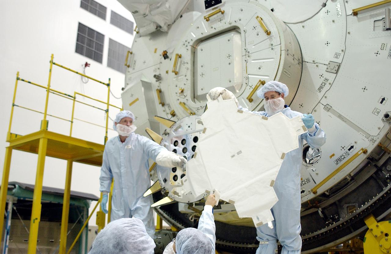 KENNEDY SPACE CENTER, FLA. - In the Space Station Processing Facility, STS-115 Mission Specialist Joseph Tanner (left) and STS-117 Mission Specialist James Reilly (right) remove a cover from the Exposed Facility Berthing Mechanism (EFBM) on the Japanese Experiment Module (JEM) behind them. Equipment familiarization is a routine part of astronaut training and launch preparations.