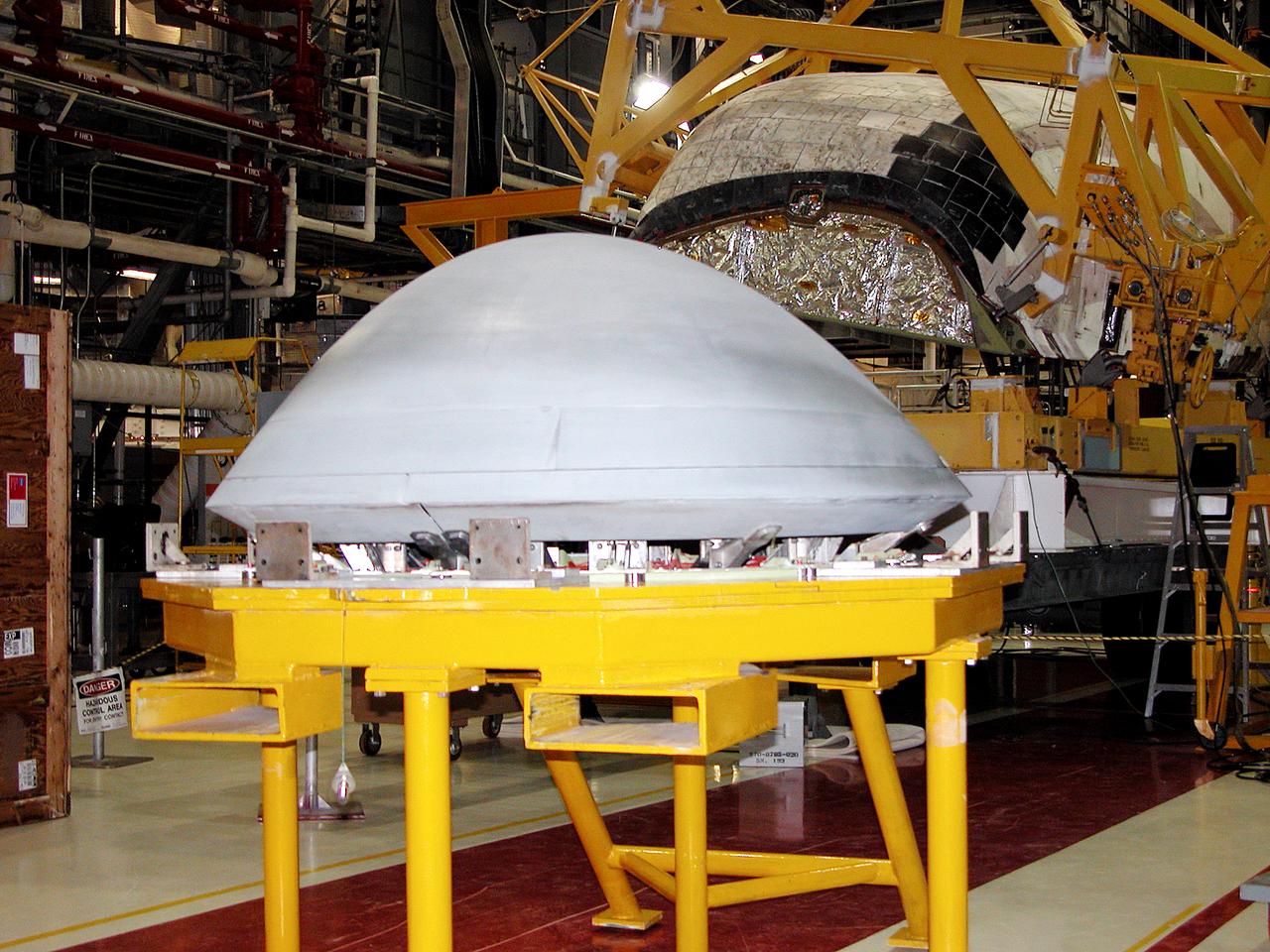 In the Orbiter Processing Facility, the nose cap (foreground) removed from Atlantis (behind) waits to be shipped to the original manufacturing company, Vought in Ft. Worth, Texas, a subsidiary of Lockheed Martin, to undergo non-destructive testing such as CAT scan and thermography.