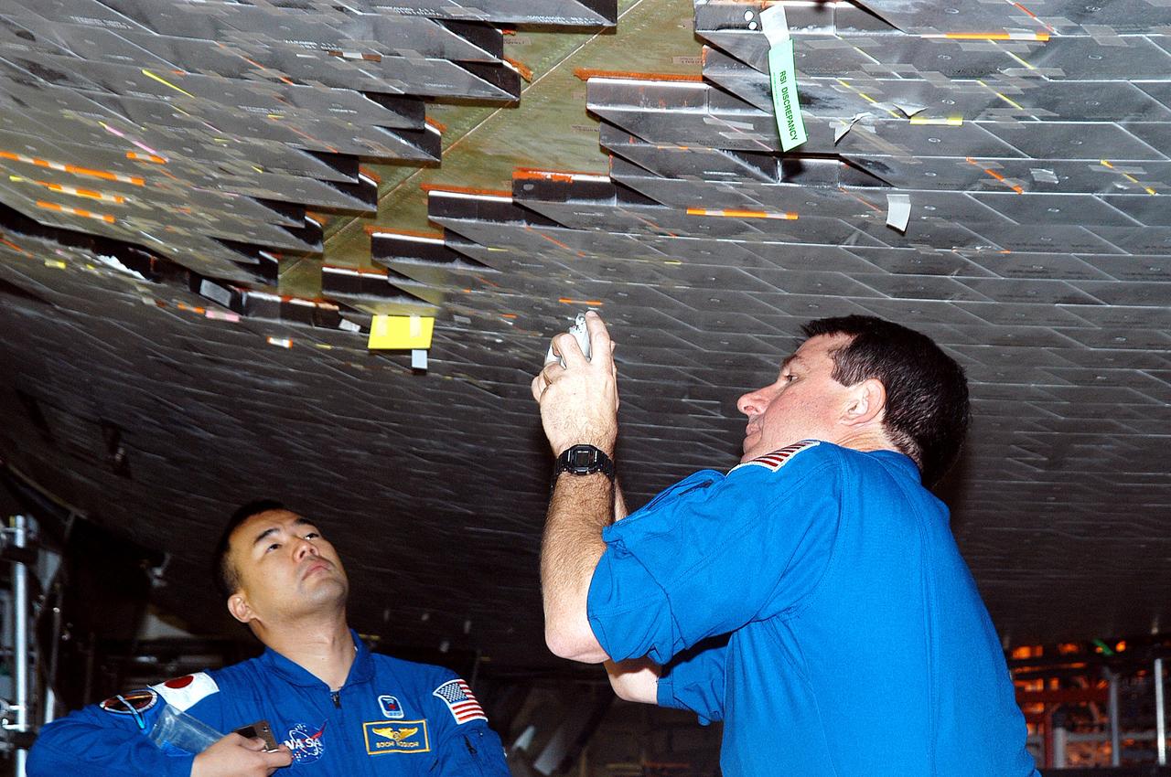 KENNEDY SPACE CENTER, FLA. -  In the Orbiter Processing Facility, STS-114 Mission Specialists Soichi Noguchi and Stephen Robinson take a close look at the some of the tiles underneath Atlantis.  Noguchi is with the Japan Aerospace Exploration Agency, JAXA.  The STS-114 crew is at KSC to take part in crew equipment and orbiter familiarization.