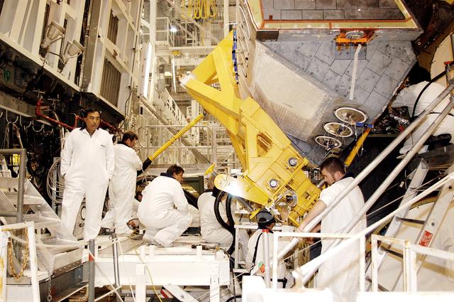 NASA image: KENNEDY SPACE CENTER, FLA. - In the Orbiter Processing Facility, technicians make final adjustments to the orbital maneuvering system (OMS) pod being installed on Atlantis.   The OMS pod is one of two that are attached to the upper aft fuselage left and right sides. Fabricated primarily of graphite epoxy composite and aluminum, each pod is 21.8 feet long and 11.37 feet wide at its aft end and 8.41 feet wide at its forward end, with a surface area of approximately 435 square feet. Each pod houses the Reaction Control System propulsion components used for inflight maneuvering and is attached to the aft fuselage with 11 bolts.