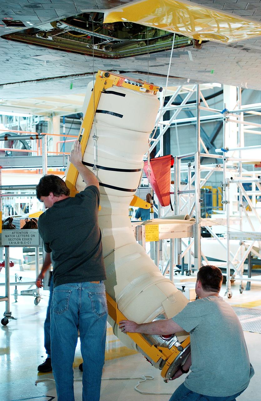 KENNEDY SPACE CENTER, FLA. -   In the Orbiter Processing Facility, workers lift the liquid oxygen feedline for the 17-inch disconnect toward orbiter Discovery for installation. The 17-inch liquid oxygen and liquid hydrogen disconnects provide the propellant feed interface from the external tank to the orbiter main propulsion system and the three Shuttle main engines.