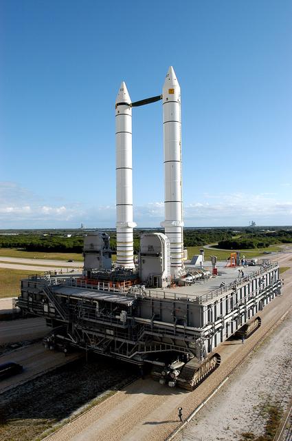 NASA image: KENNEDY SPACE CENTER, FLA. -  The crawler transporter slowly moves the Mobile Launcher Platform (MLP), carrying a set of twin solid rocket boosters, away from the Vehicle Assembly Building (VAB) in support of engineering analysis vibration tests on the crawler and MLP.  On either side of the boosters on the horizon can be seen the two launch pads. The crawler is moving at various speeds up to 1 mph in an effort to achieve vibration data gathering goals as it leaves the VAB and then returns.  The boosters are braced at the top for stability.  The primary purpose of these rollout tests is to gather data to develop future maintenance requirements on the transport equipment and the flight hardware. Various parts of the MLP and crawler transporter have been instrumented with vibration data collection equipment.